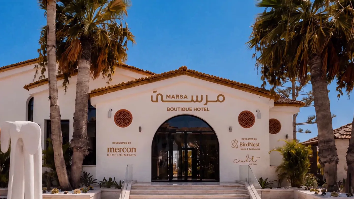 The frontage of Marsa Boutique Hotel, white stucco under a terracotta tiled roof between the palms
